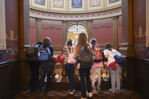A group of six preteen students inside the Michigan Capitol building look over the railing in the dome.