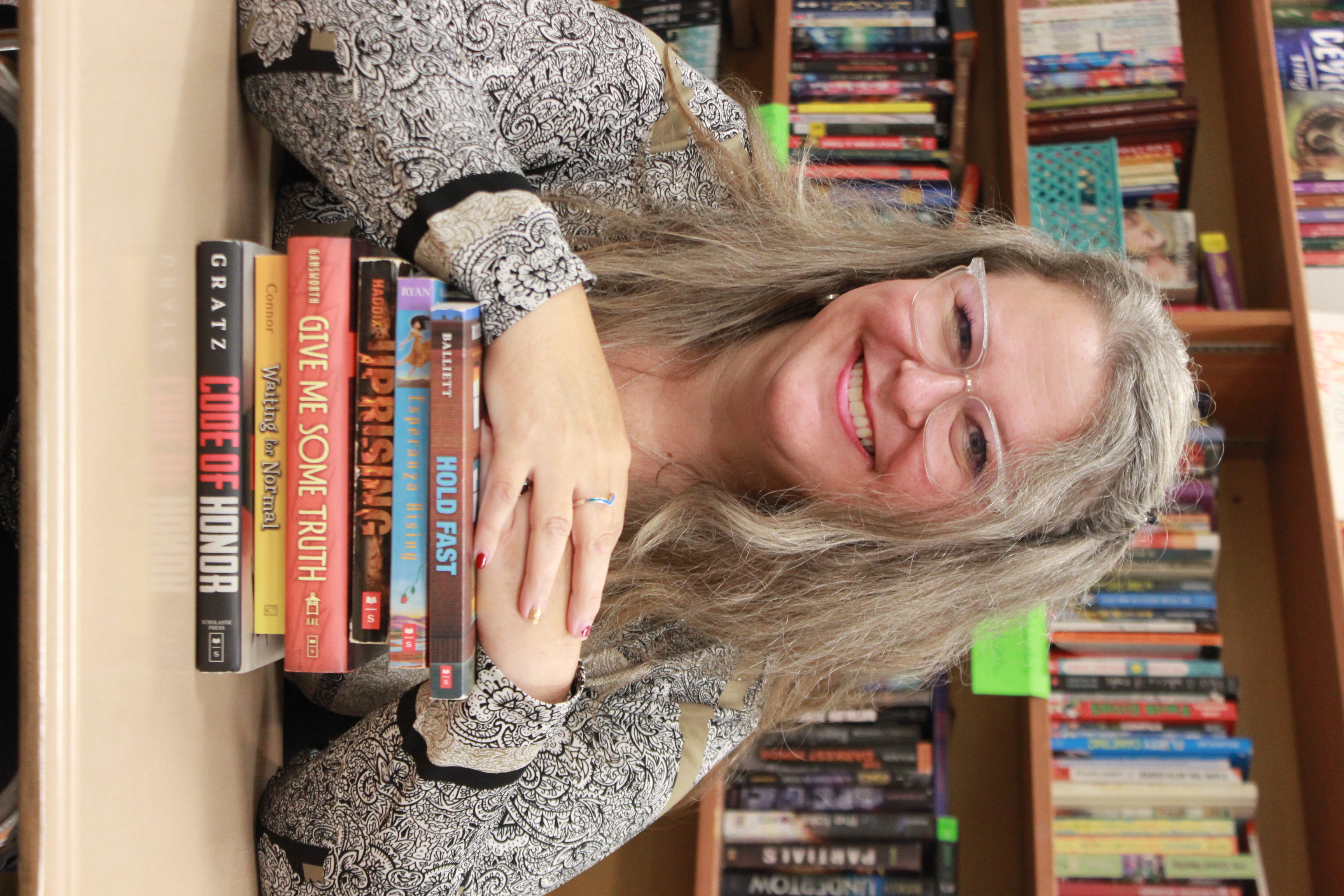Debbie Carew smiles while resting her hands on a stack of books