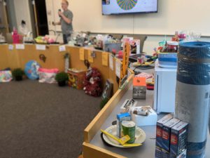 Semi-circle board table filled with prizes. Out-of-focus man in back with microphone announcing prize winners.